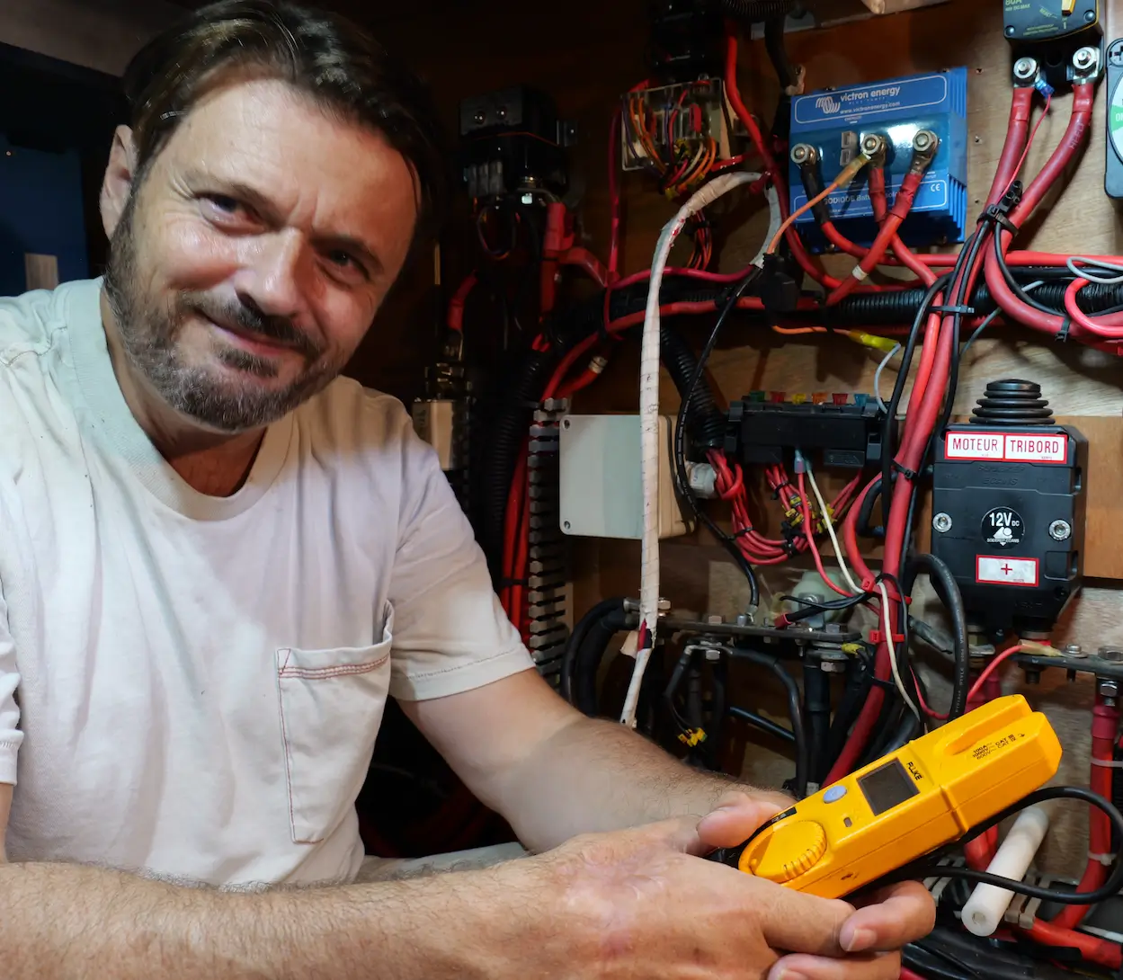 Man holding an electrical test instrument beside a boat’s electrical installation