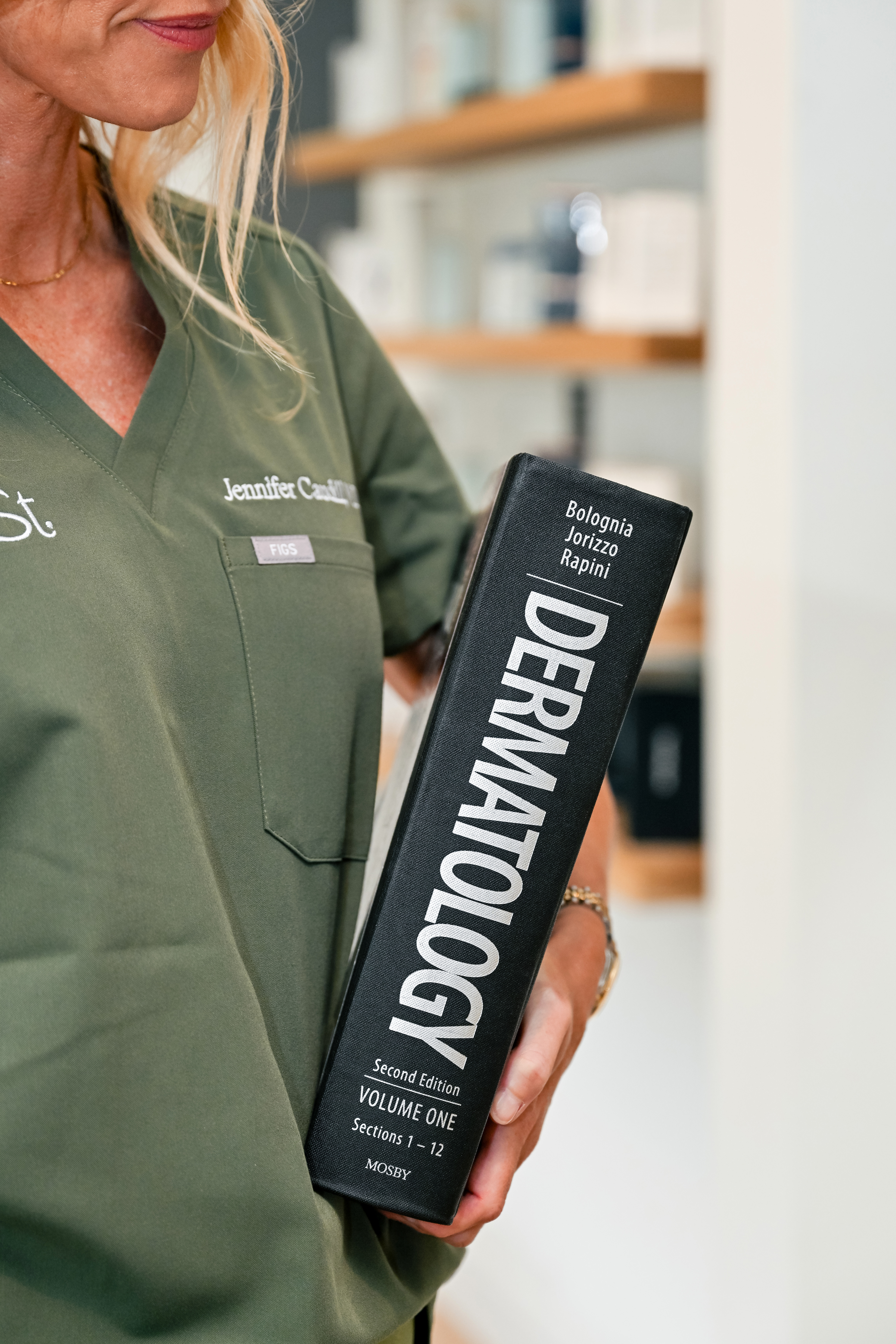 Main Street Dermatology provider in professional attire holding the Bolognia Dermatology textbook