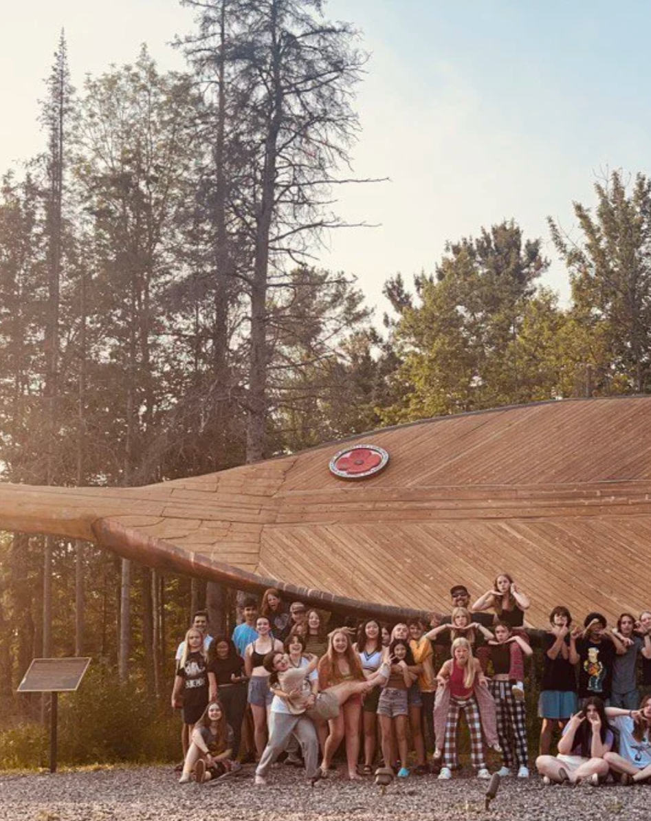A group of adolescents outside a timber building among tall trees