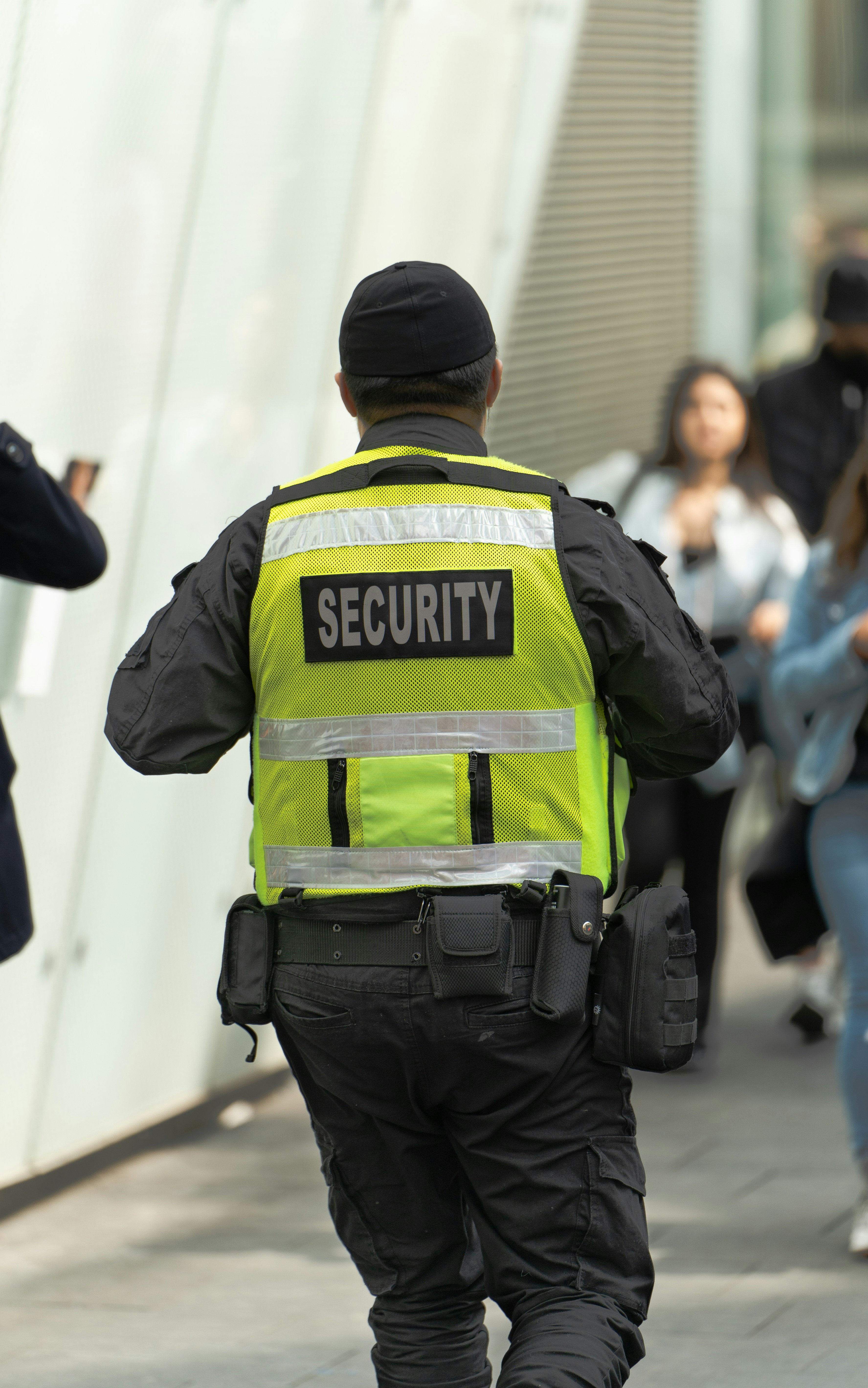Security officer in a high-visibility vest walking along a city street, seen from behind