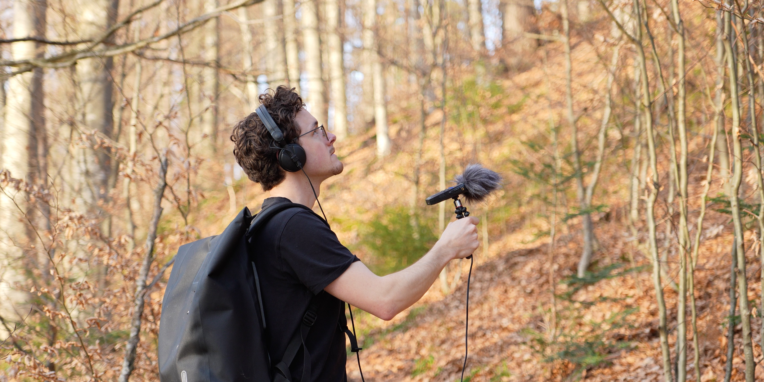 Jonas Fasching field recording in an autumn forest, holding a recorder with headphones on