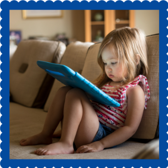 Child using a tablet while sitting on a couch.