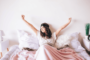 A woman wakes up in a pink bed feeling refreshed because she learned how to go to bed earlier