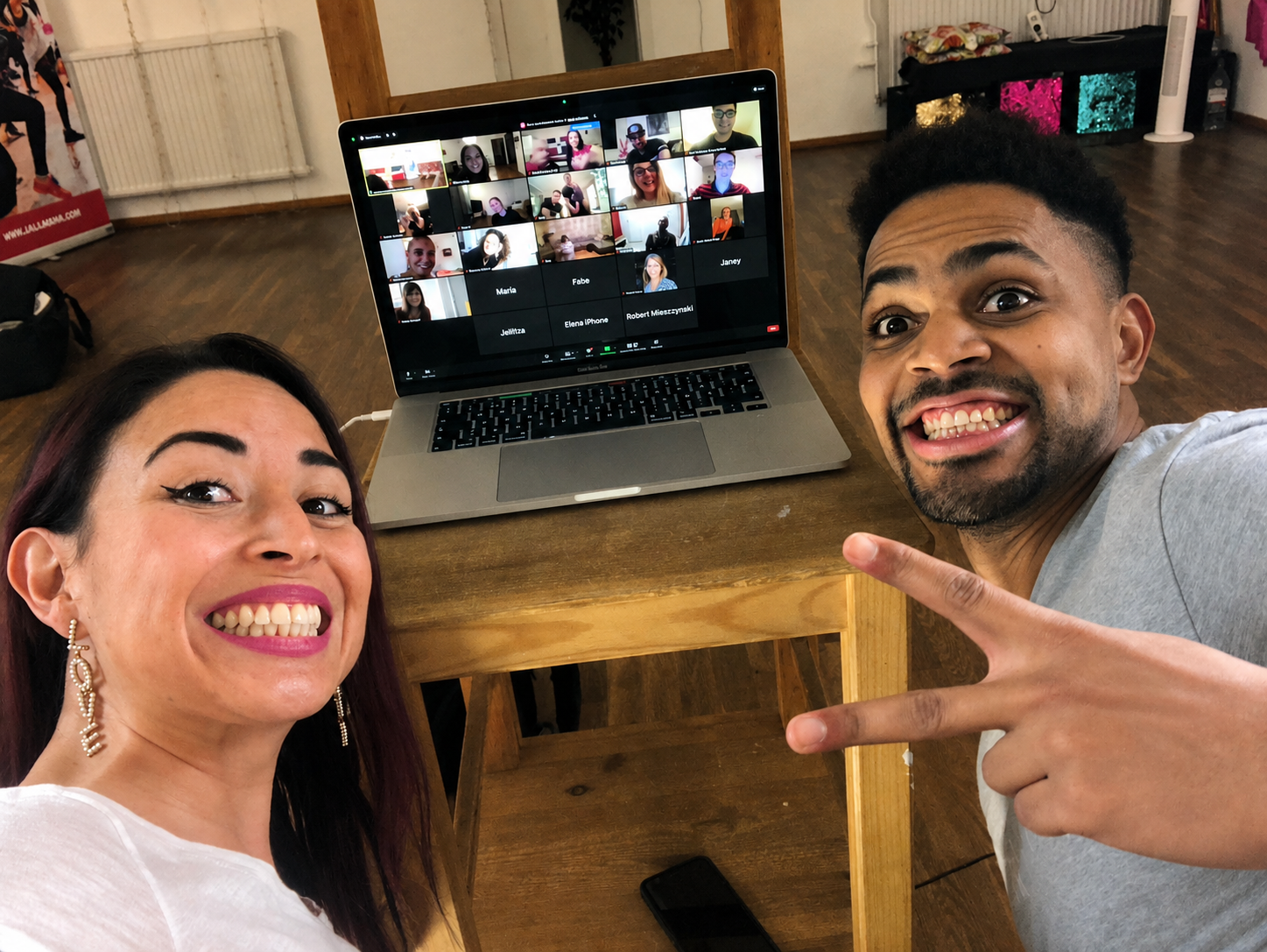 Junior and Carolina posing with the PC, where you can see their online students smiling through Zoom