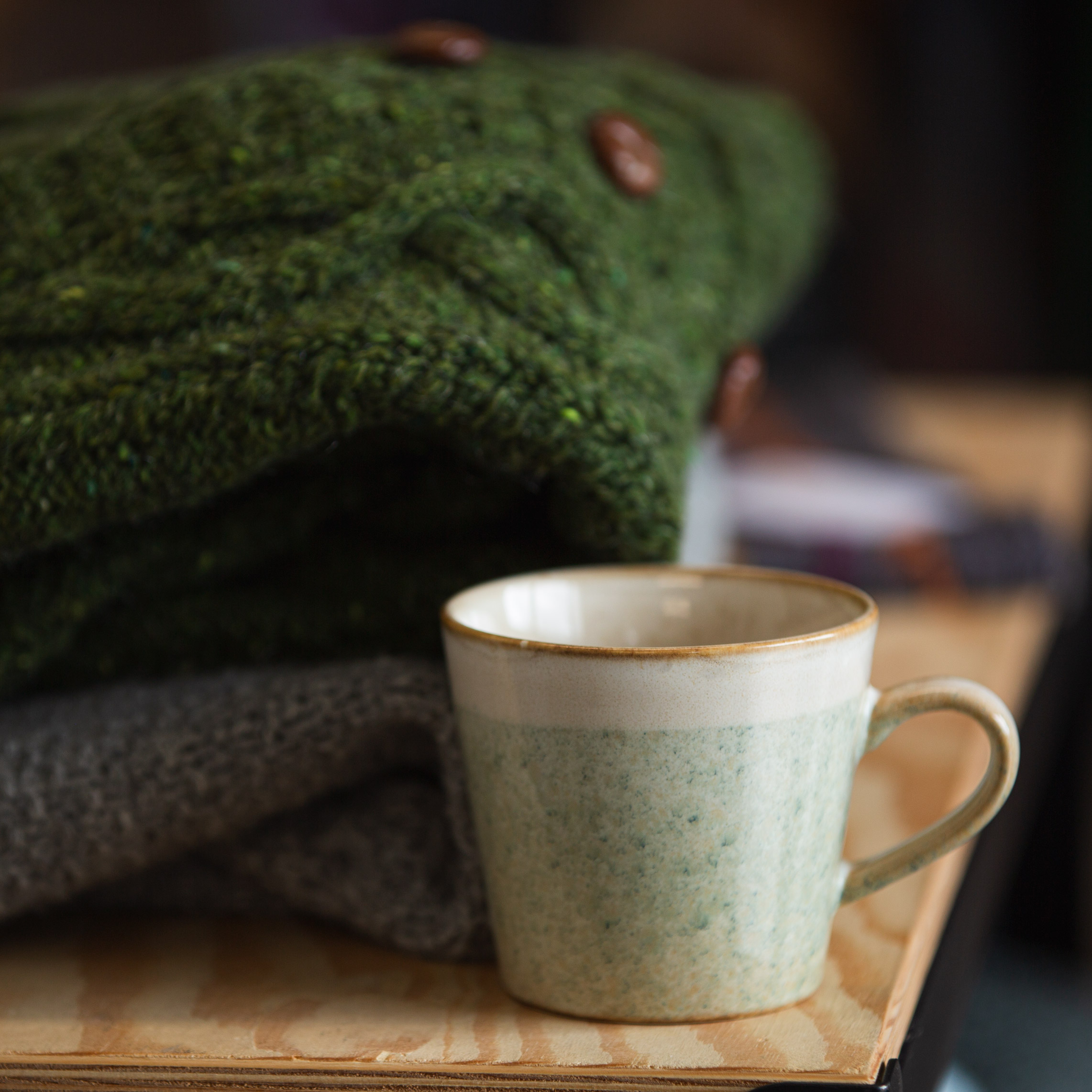 A cup sat on a table next to a pile of knitted sweaters.