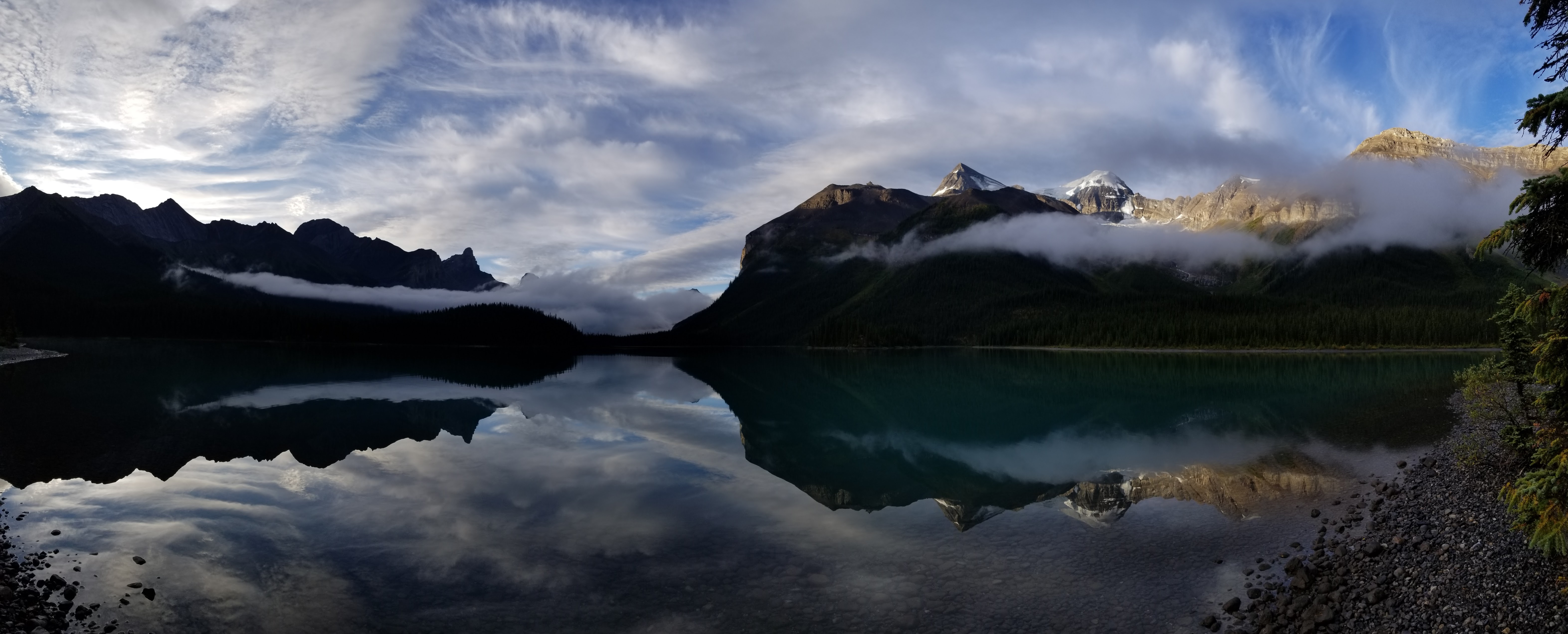 A person sits in a canoe on a bright blue lake next to a large mountain, the sun shining in the background.