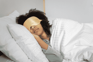 A bedtime procrastinator is in bed early with a gold sleep mask on