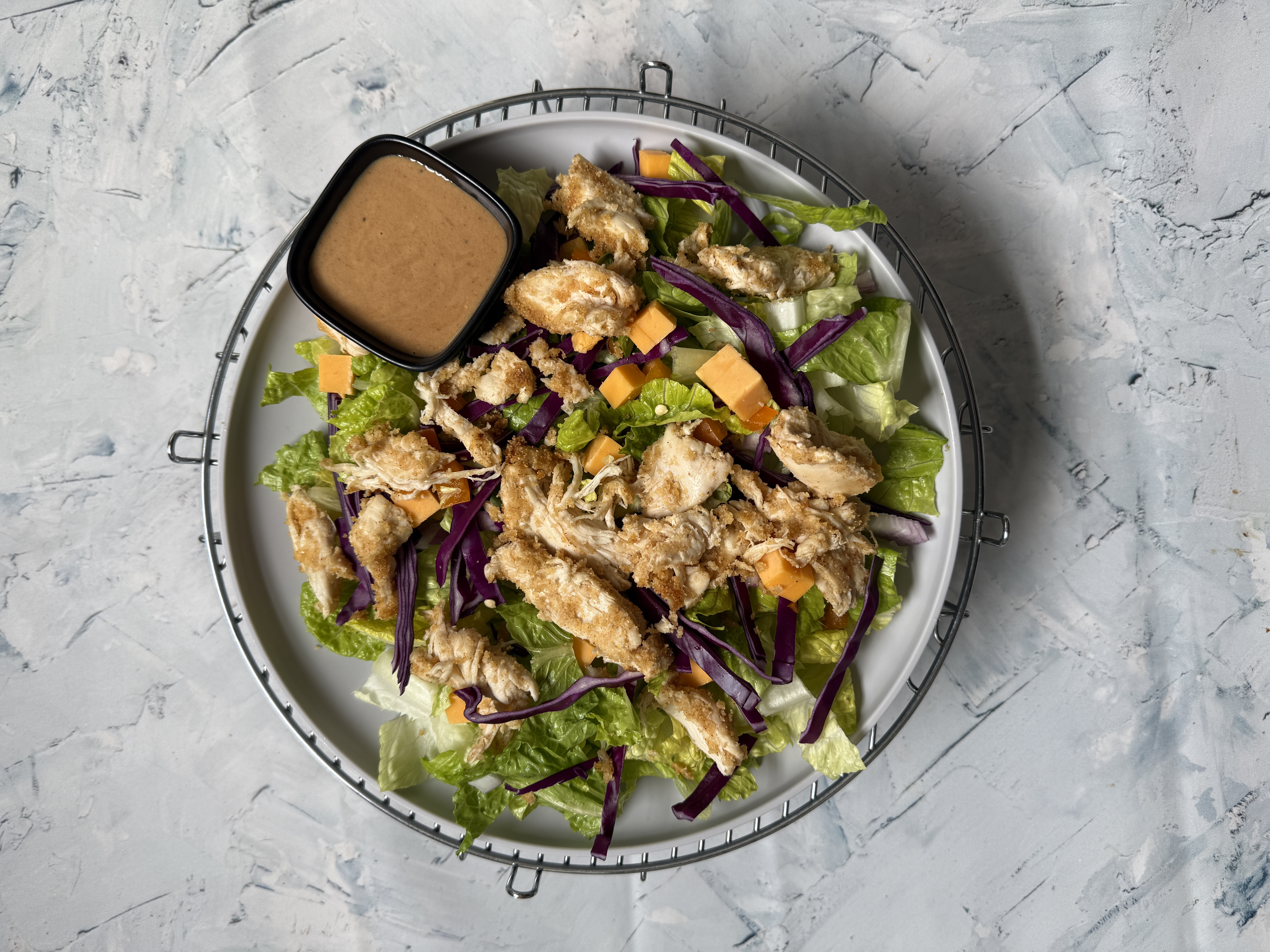 plate of salad with chicken, cheese, and greens with cup of dressing
