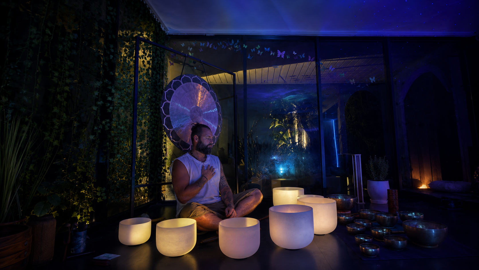 Facilitator playing singing bowls in a candlelit room, opening sacred space for a group
