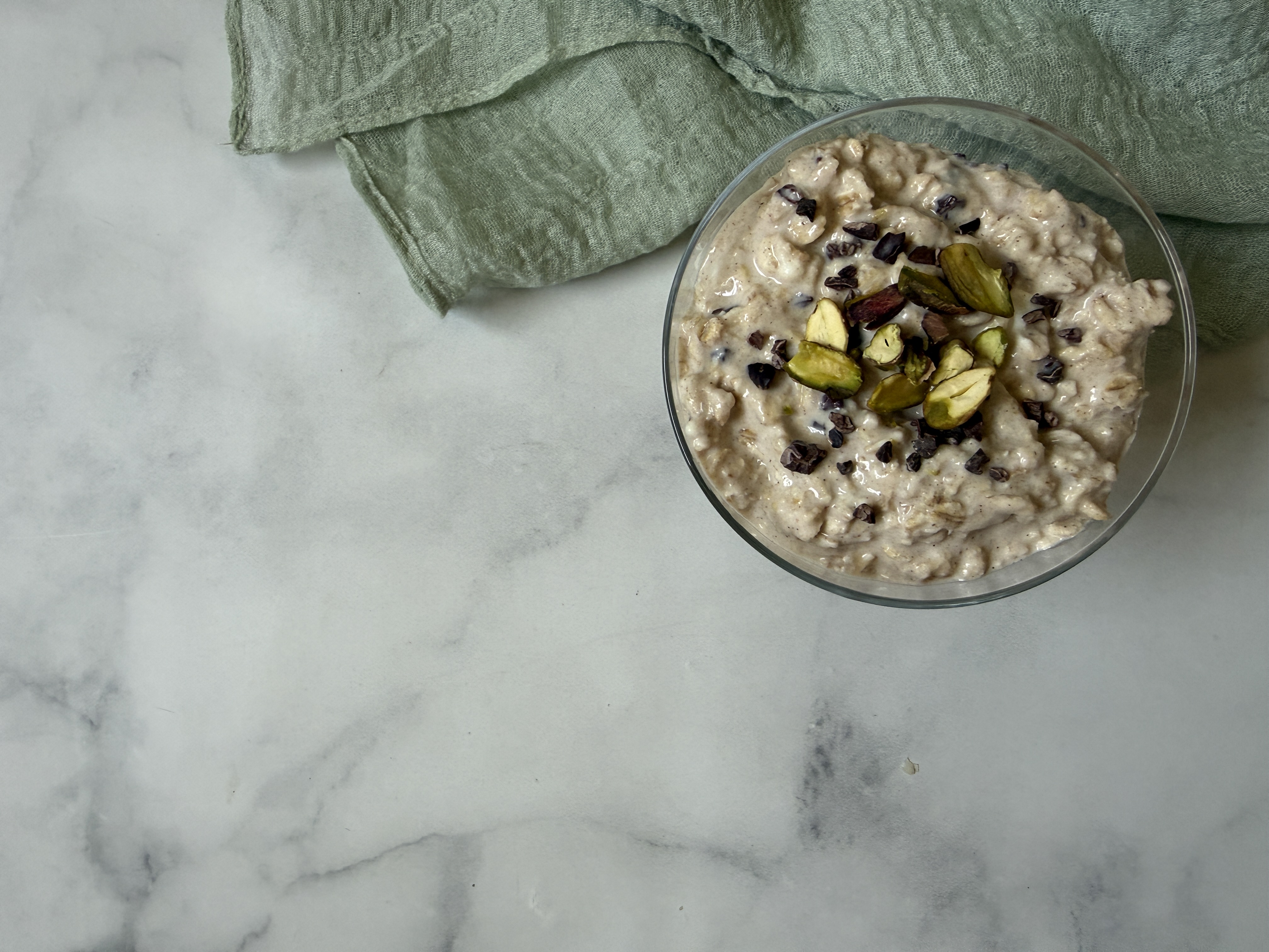 bowl of oats with nut and other toppings on marble counter with green napkin