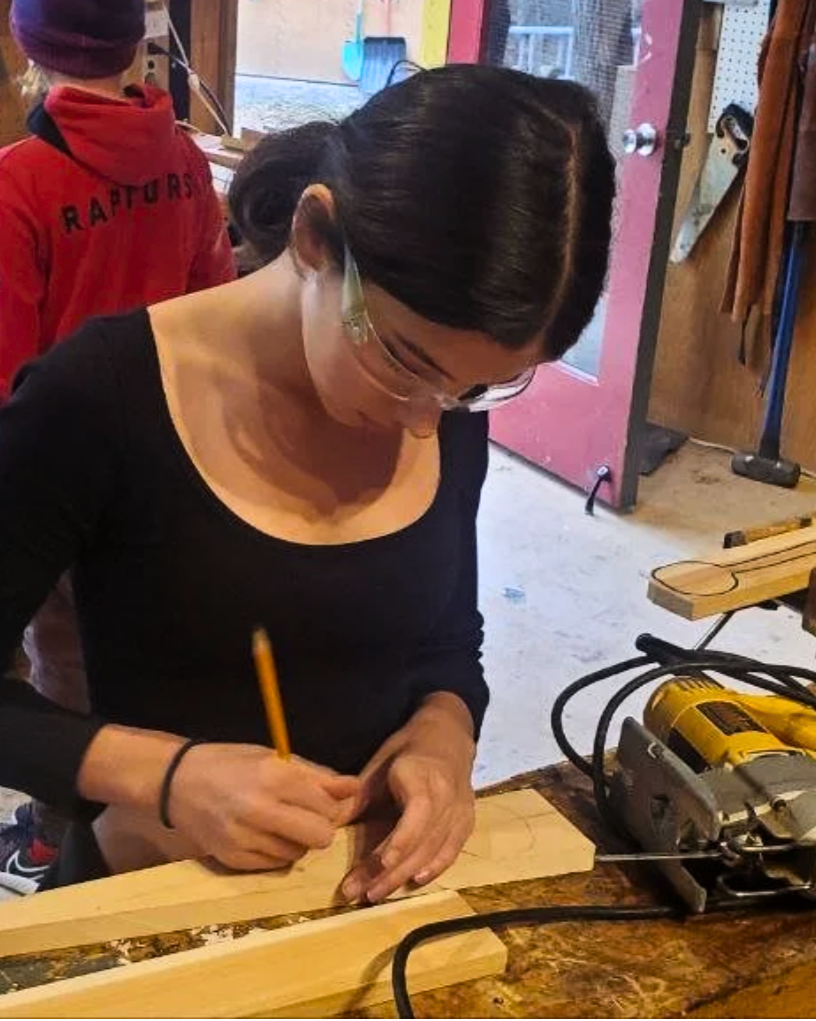 An adolescent measuring and marking a piece of wood in a workshop
