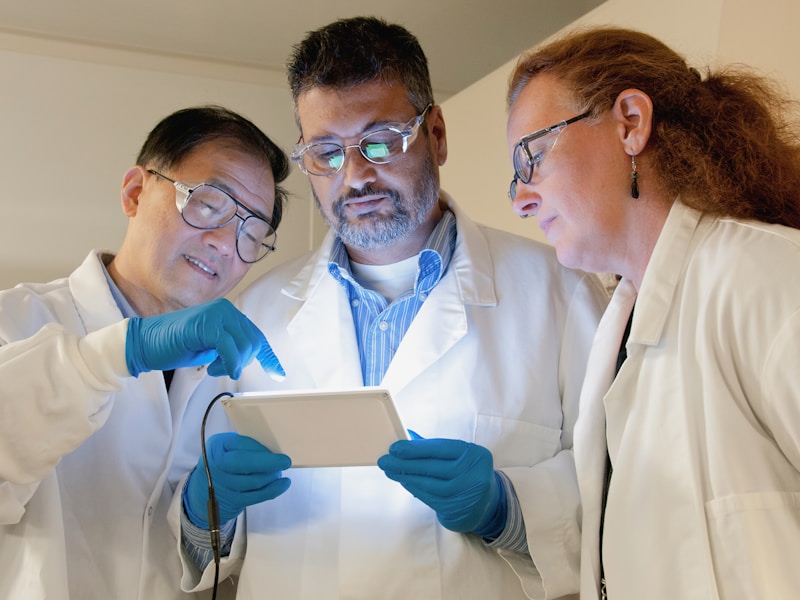 Three researchers in lab coats reviewing data together on a tablet