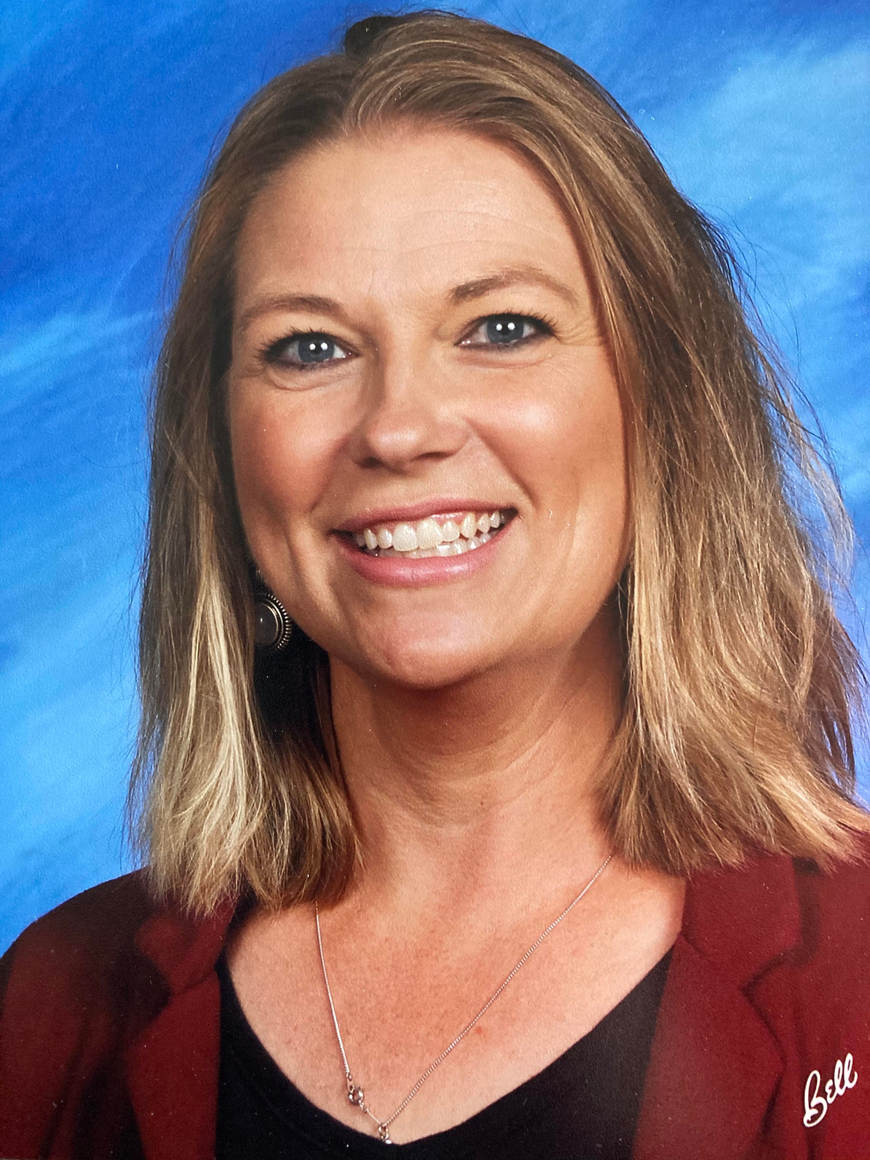 Smiling Women with jewelry, shirt and business jacket on. Plain blue colored background