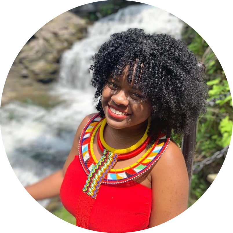 African woman with curly hair in a red dress with beaded necklace in front of a waterfall