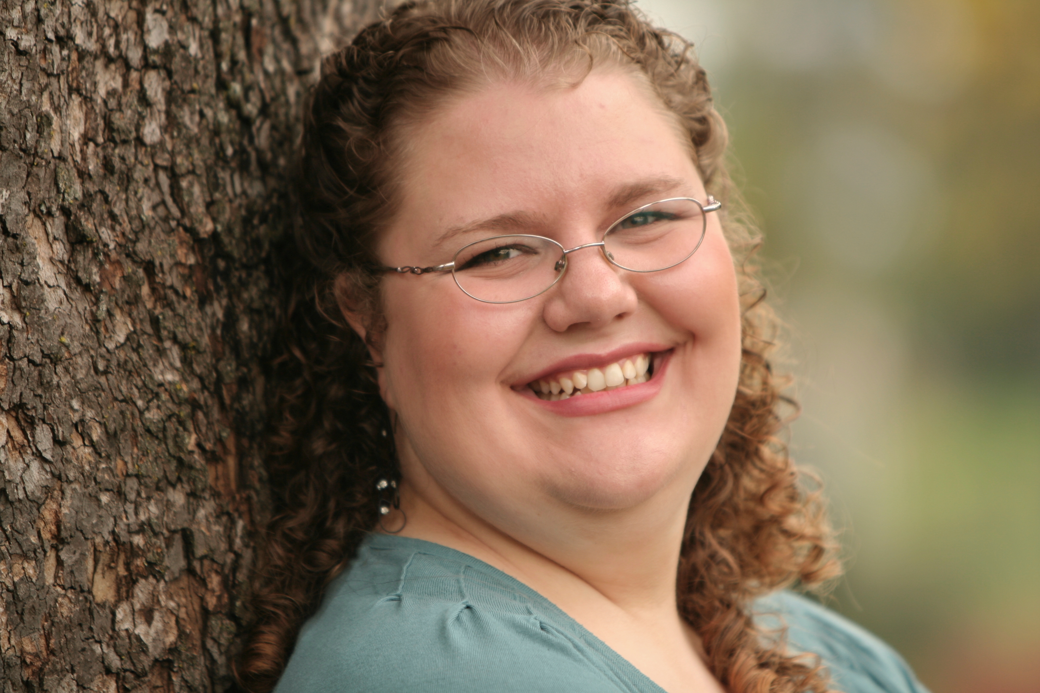 Woman smiling while resting her back against a tree