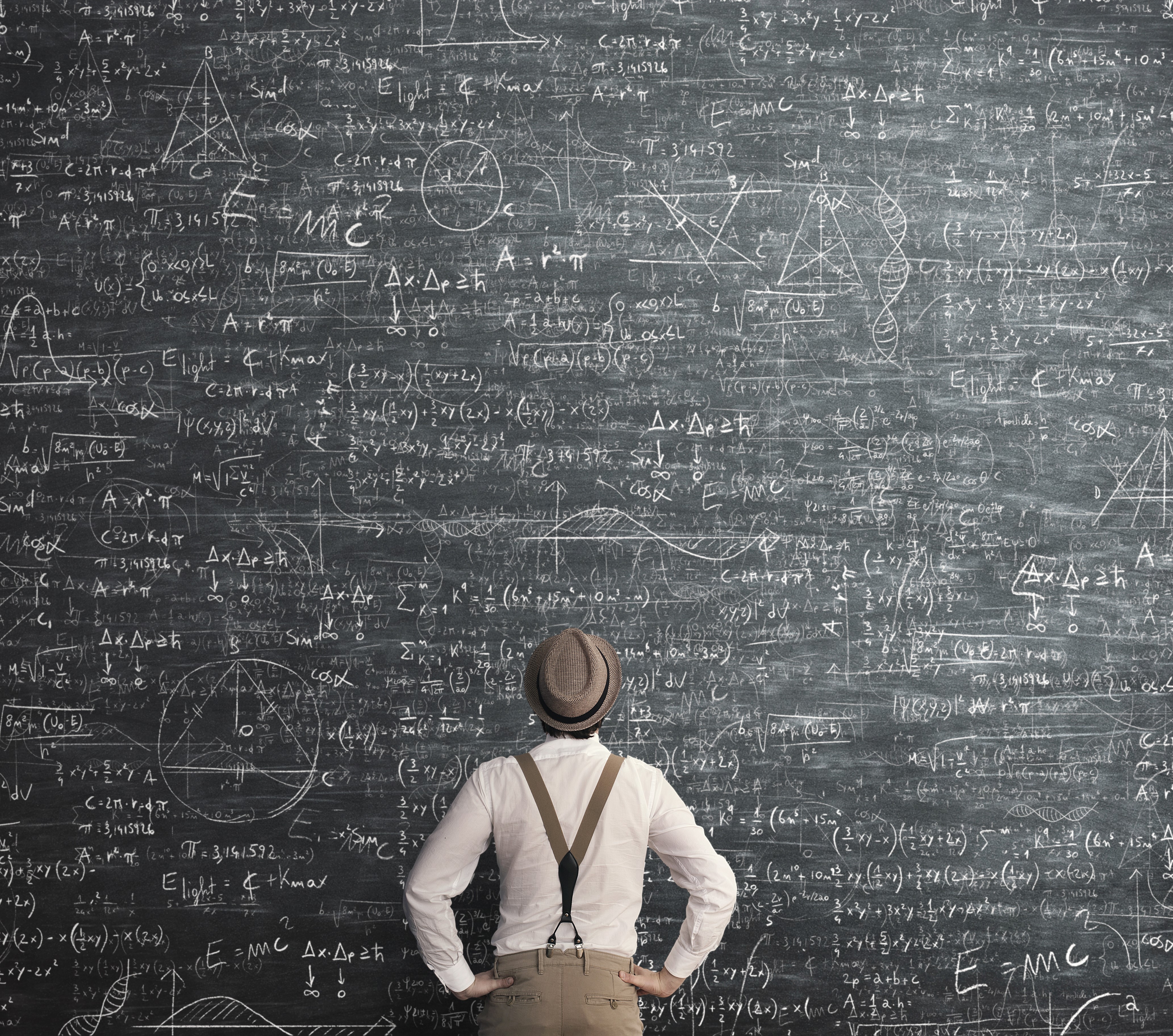 A large black board in a lecture hall. It is covered with complex equations and there is a person looking up at it with his hand on his hips. He looks very confused. Suggesting that the Public Adjuster Exam is quite difficult.