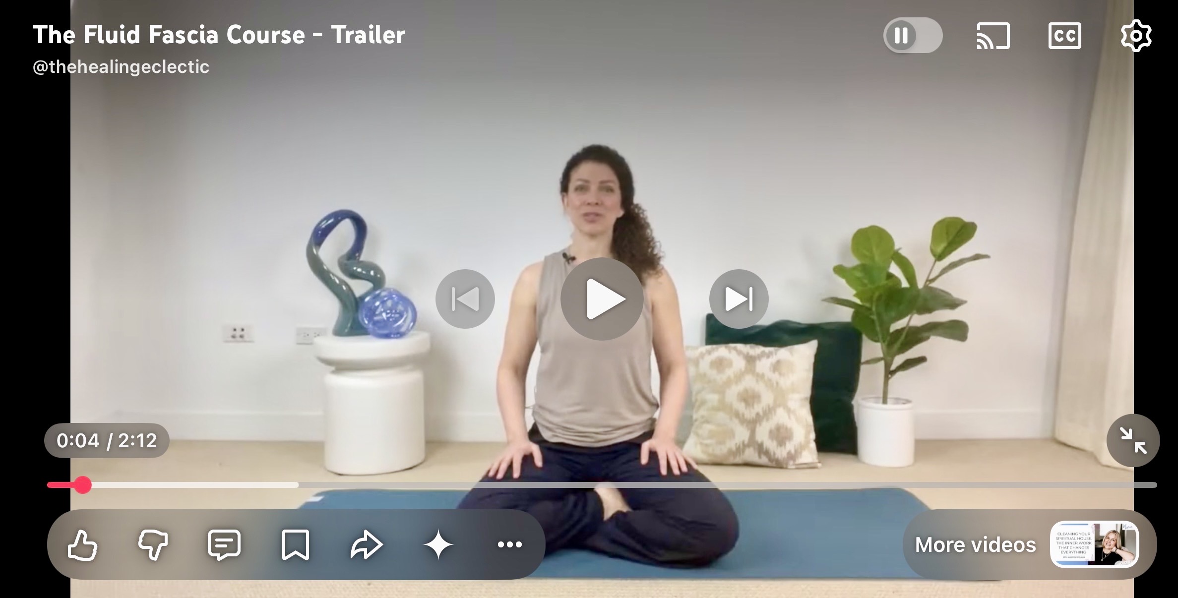 The Fluid Fascia YouTube Trailer image with woman seated cross legged on a teal yoga mat wearing a tan colored tank top, navy blue pants.  Blue way statue on a white table, two pillows and a green floor plant behind her.