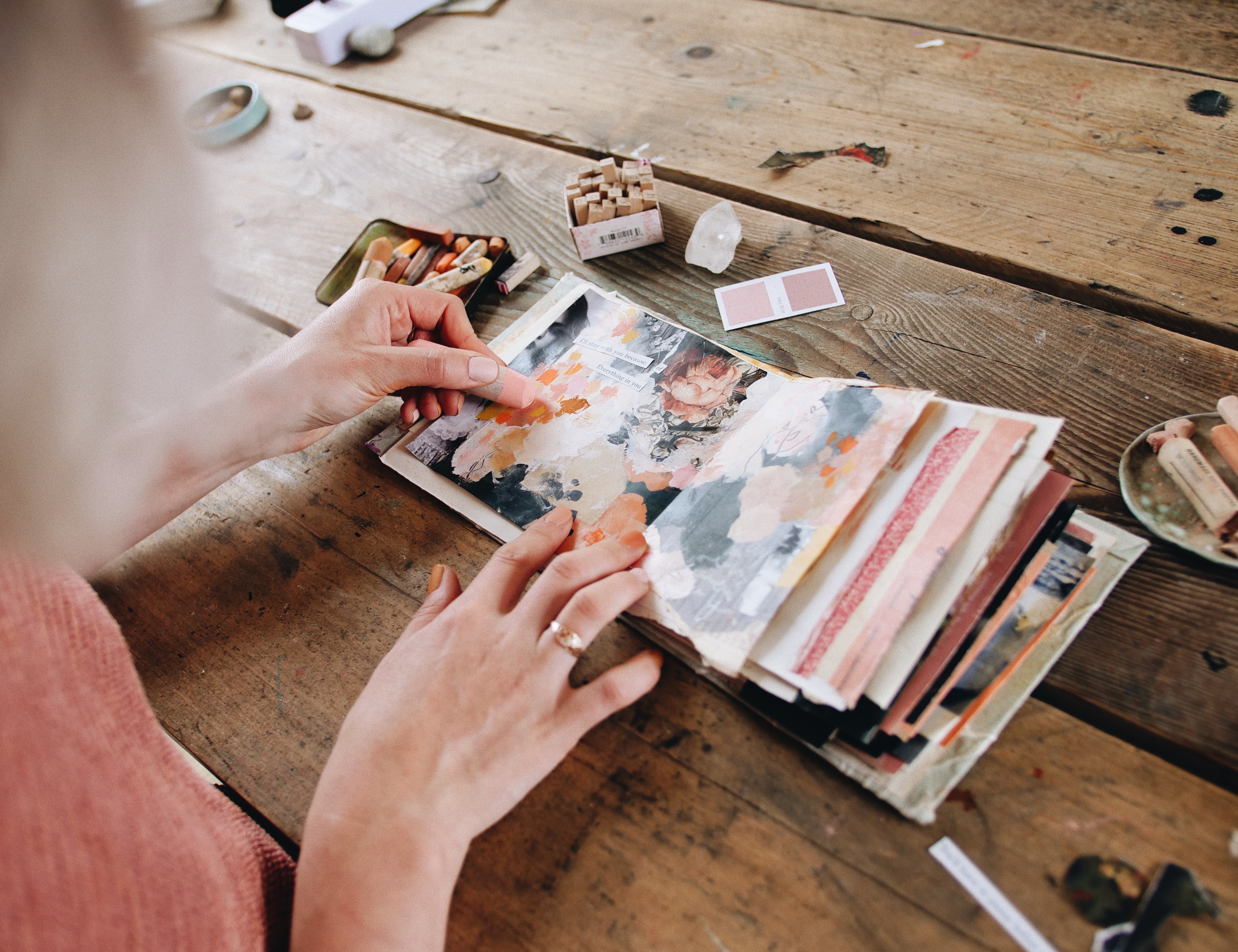 A table with mixed-media supplies used in art journaling and abstract art. Acrylic paints, watercolour paints, inks, pastels, ecolines, collage papers, paintbrushes, old photographs, art journals, washi tape, stencils, stamps.