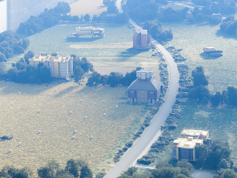 Architectural aerial visualization with scattered buildings beside a winding road and a long ribbed wall.