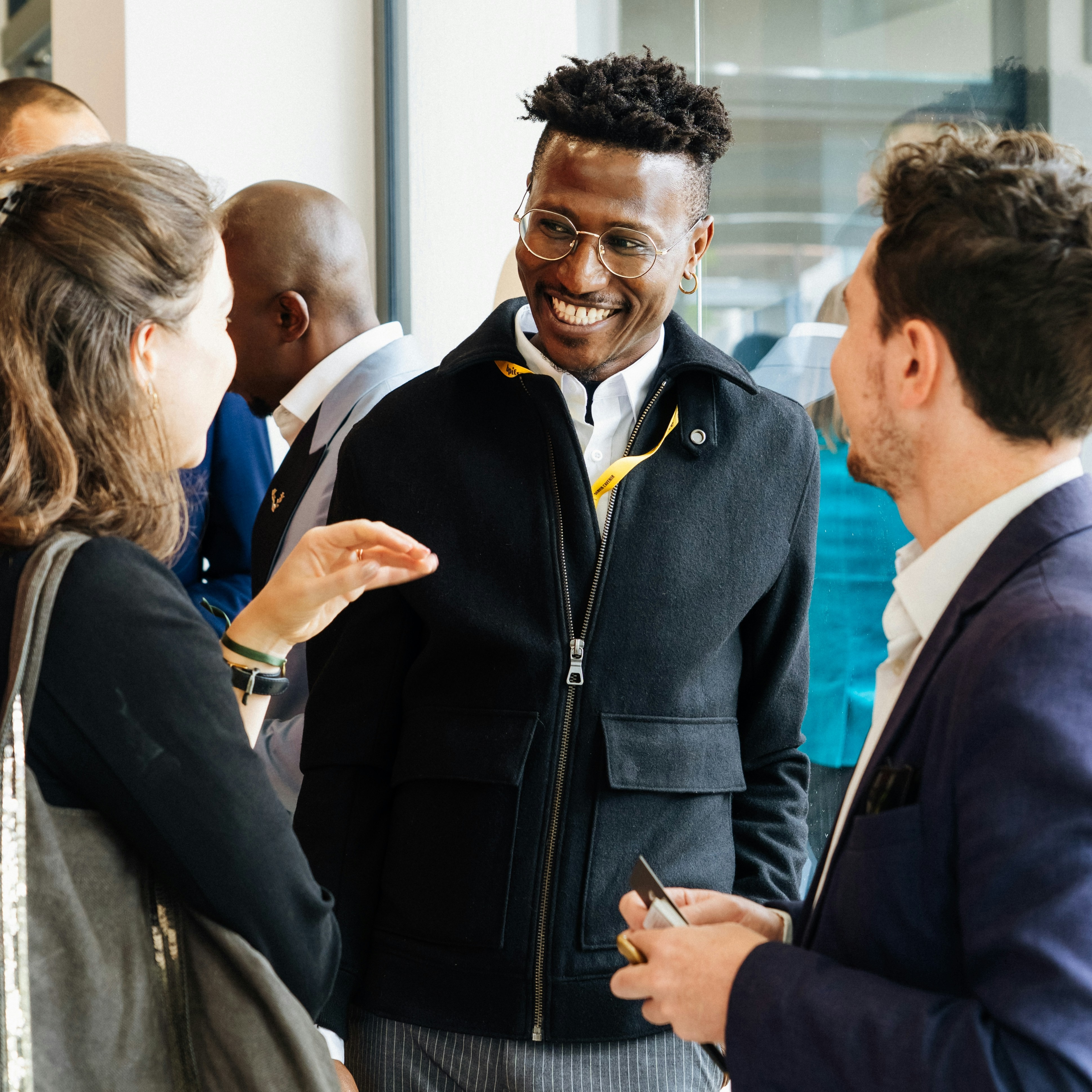 Three people smile and talk together at a busy indoor event.