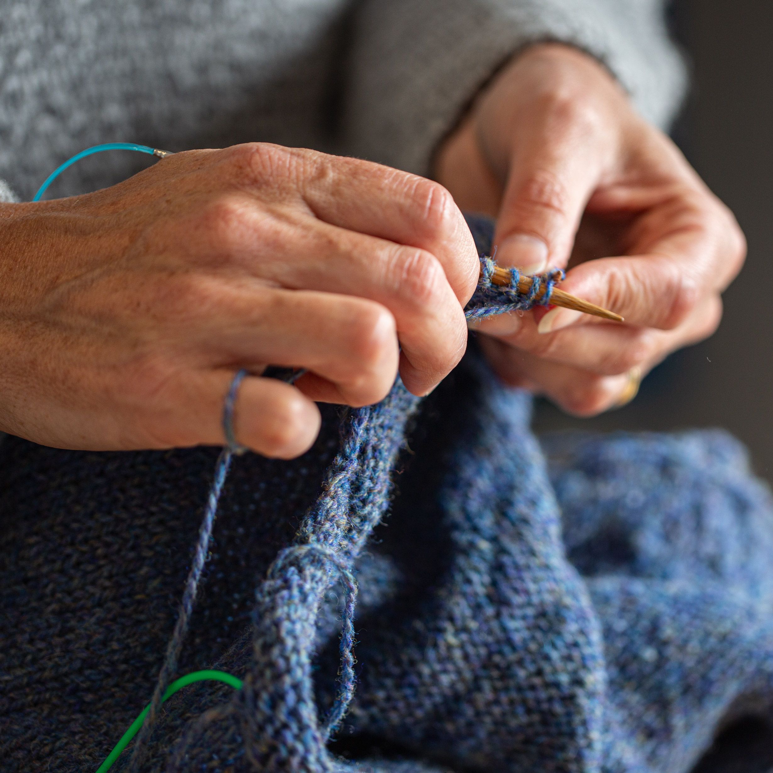 Hands knitting a blue knitting project.