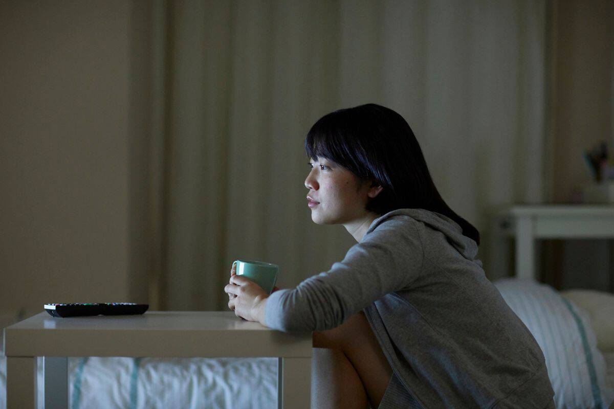A bedtime procrastinator sits next to her bed watching TV late at night