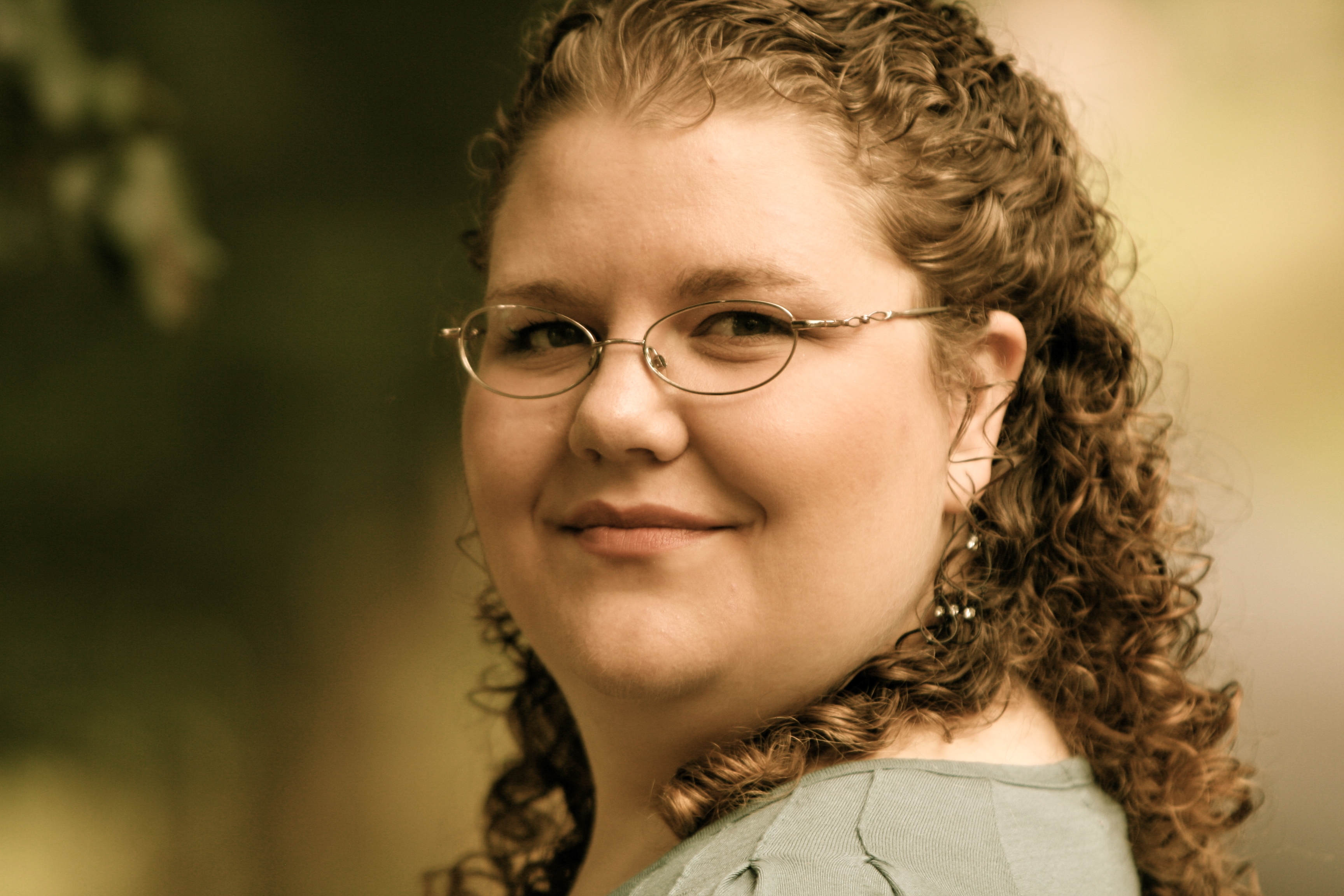 Rachel Andersen (a Caucasian woman with golden curly hair, glasses, and a round face) against a blurry background with trees
